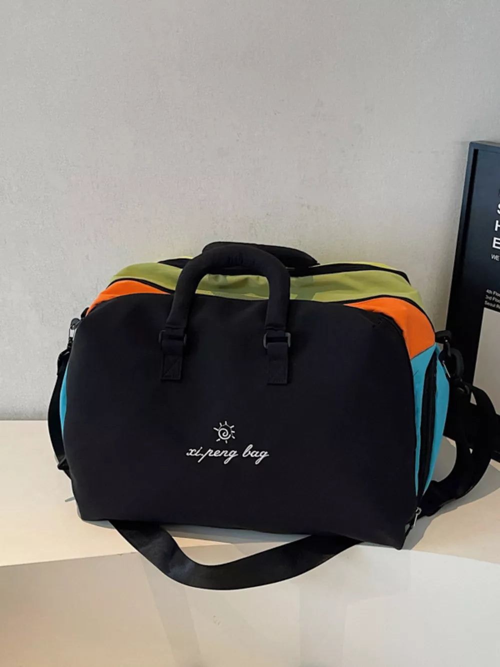 Vibrant duffel bag with black, orange, green, and blue panels and embroidered text.