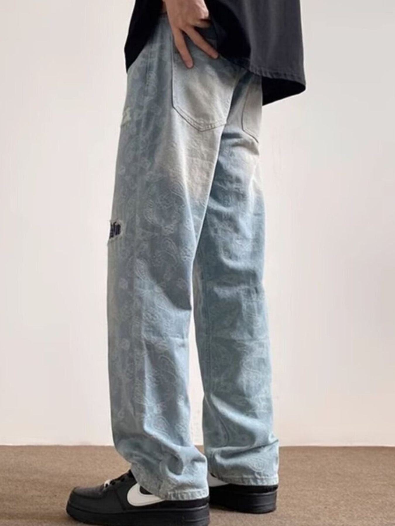 Men's light blue distressed wide-leg jeans with paisley pattern and pocket detail.