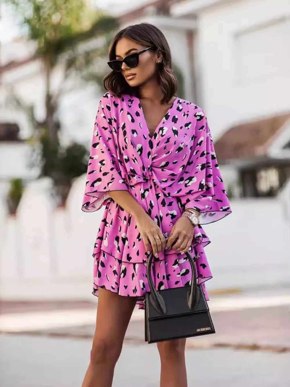 Fuchsia pink tiered mini dress with black leopard print, V-neck, flutter sleeves, and tie waist.