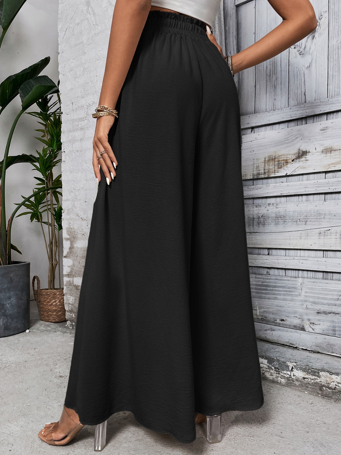Black ruffled waistline palazzo trousers with a wide leg and textured fabric.