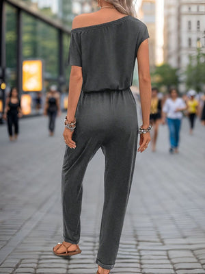 Dark gray asymmetric drape jumpsuit with drawstring waist and short sleeves.
