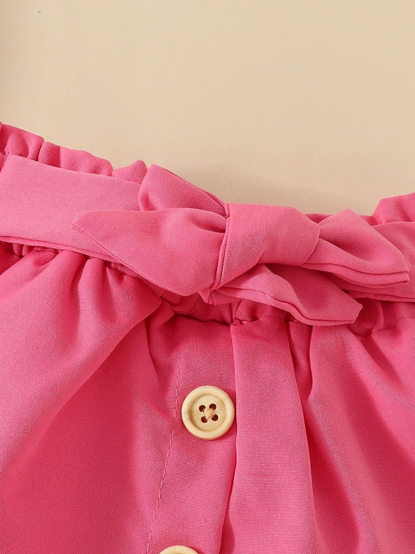 Pink baby set with ruffled waist, bow detail, and wood buttons.