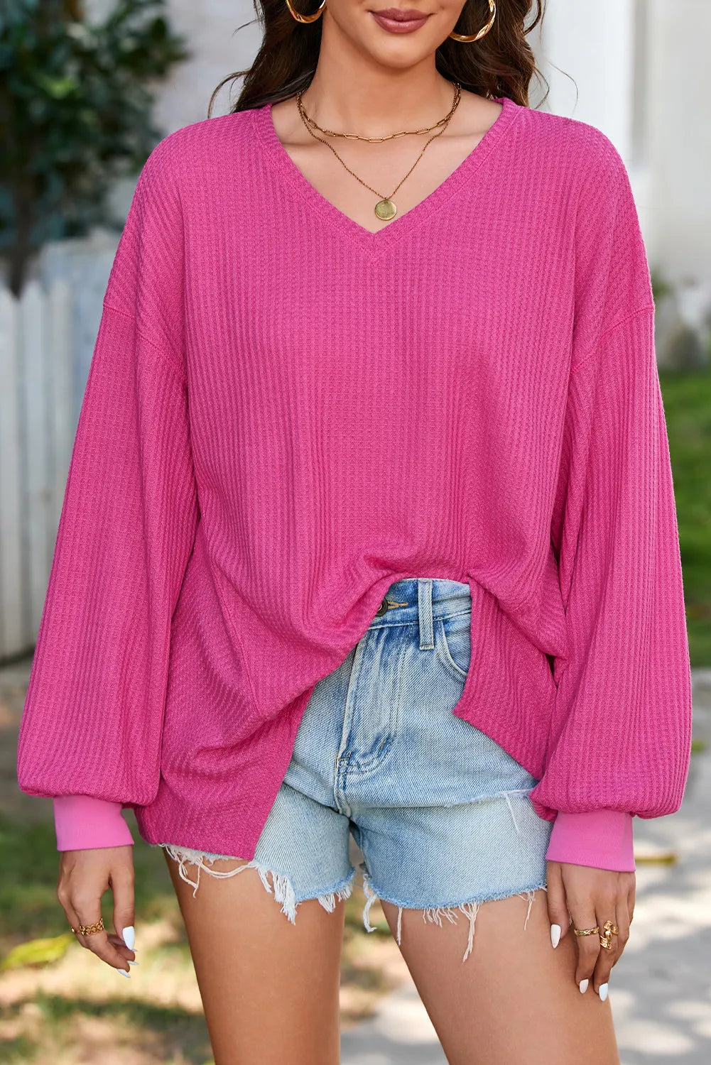 Fuchsia pink waffle knit blouse with blouson sleeves and v-neck, styled with denim shorts.
