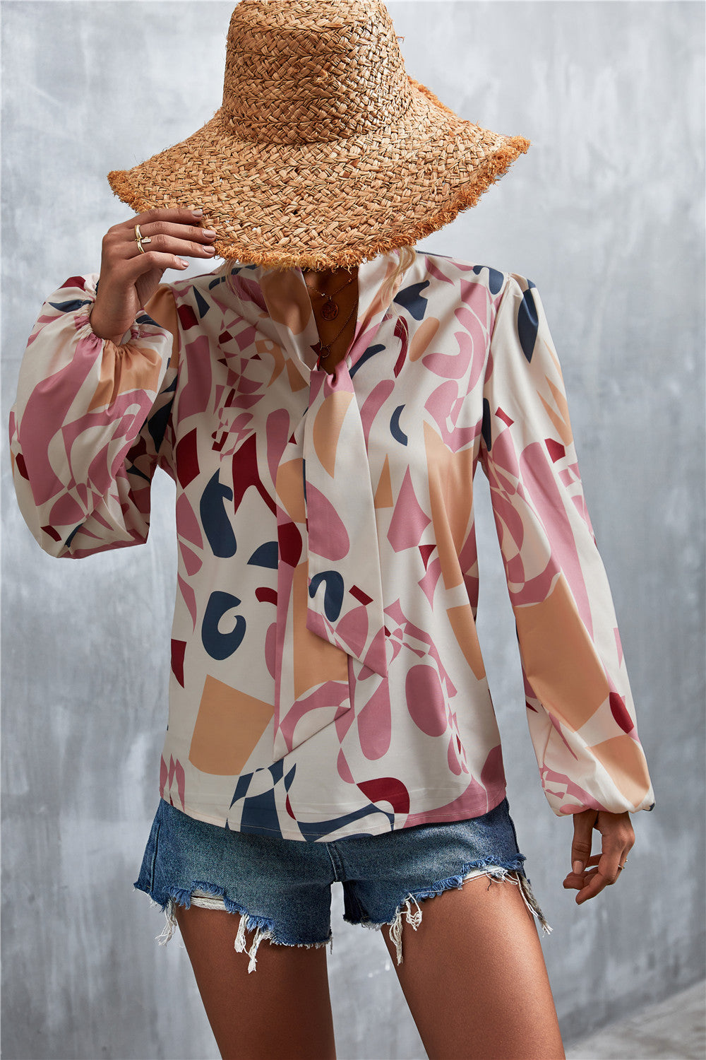 Abstract print pussy bow blouse with balloon sleeves in pink and cream with geometric shapes.