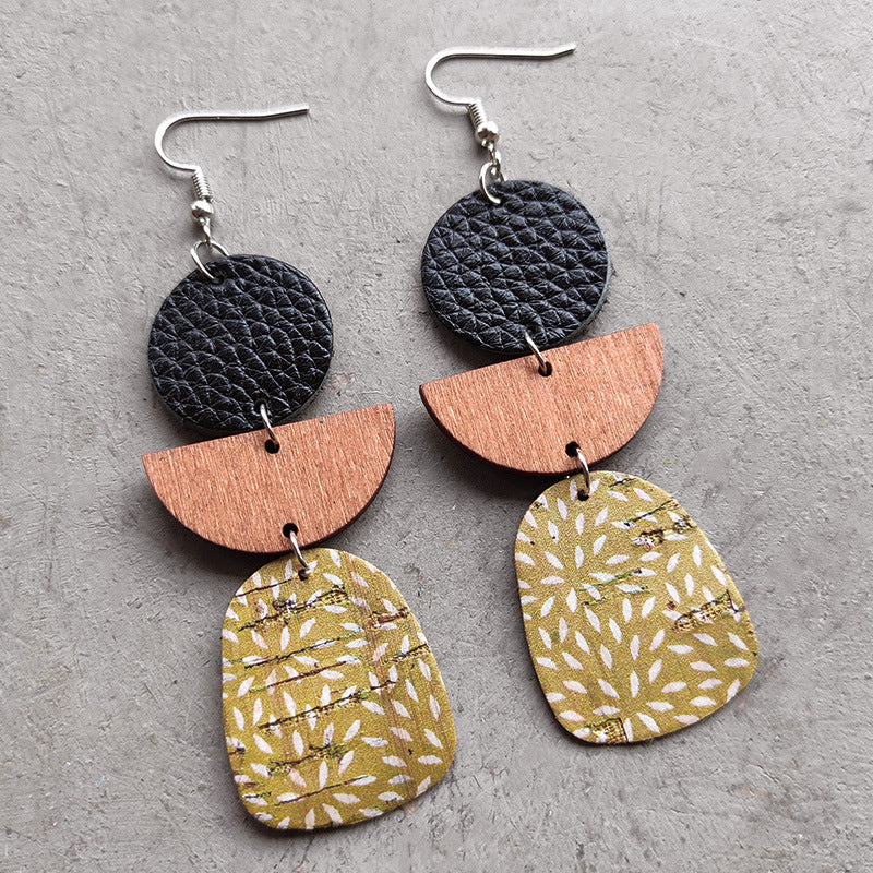 Geometric layered earrings in black leather, wood, and patterned cork with white floral design.