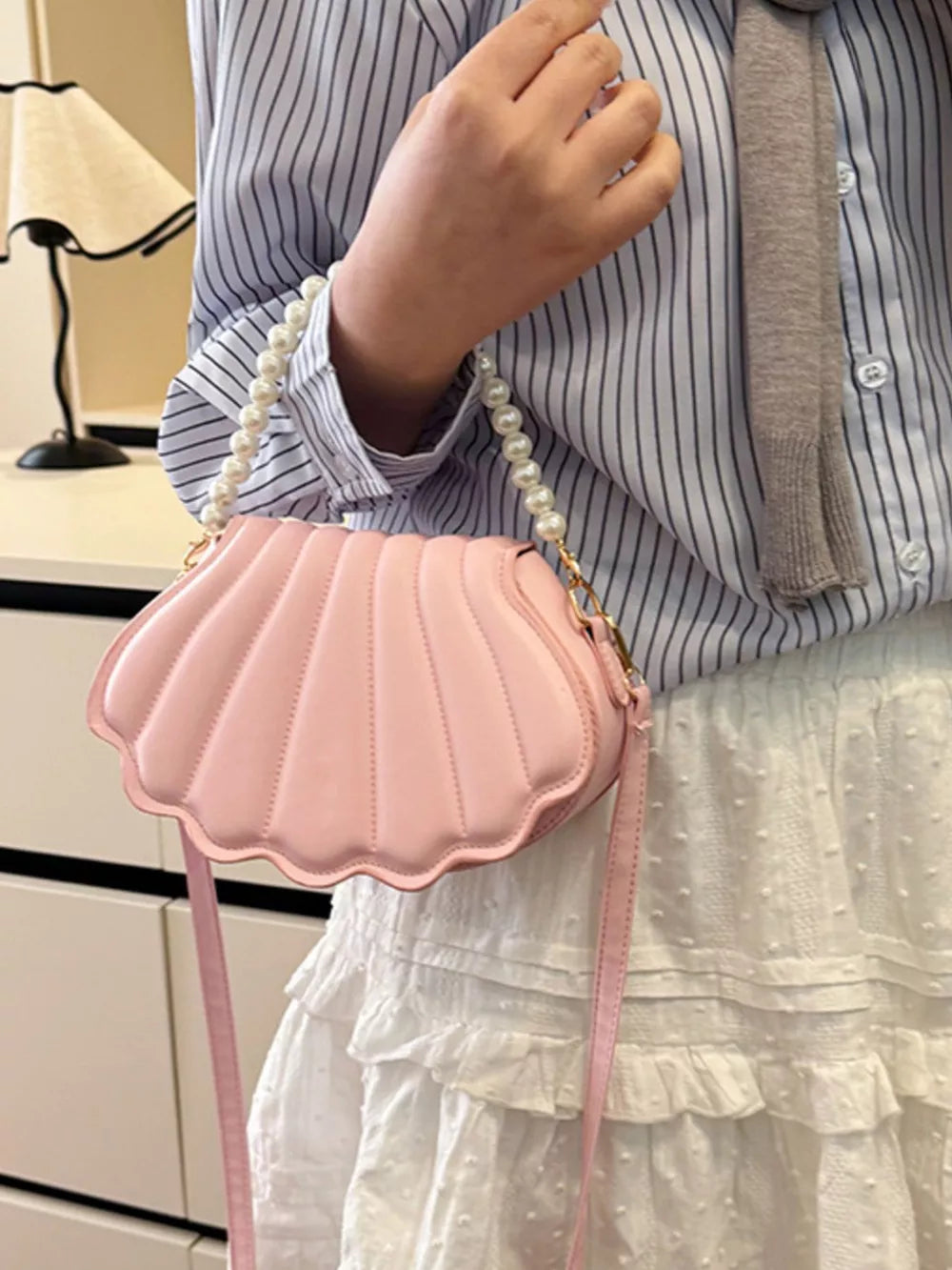 Pink shell crossbody bag with pearl strap and scalloped trim.