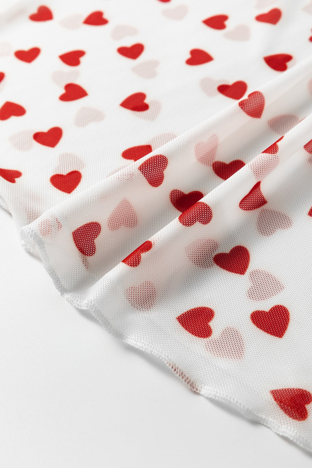 Sheer white t-shirt with red heart print, close-up detail of mesh fabric.