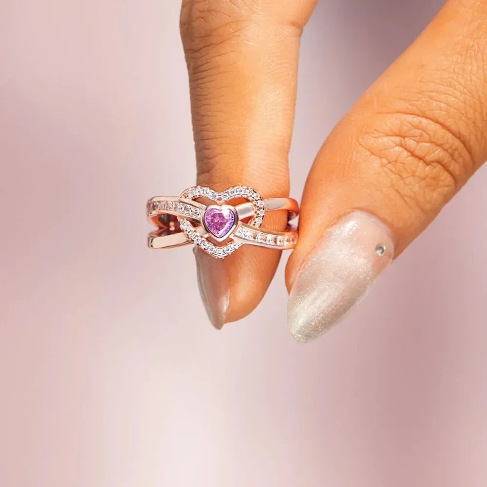 Rose gold ring with intertwined hearts, pink center stone, and clear cubic zirconia accents.