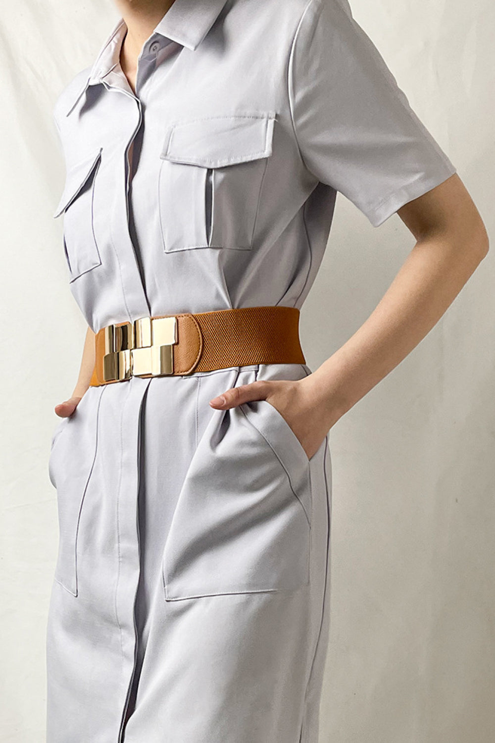 Caramel elastic belt with geometric gold buckle, cinching a light gray dress.