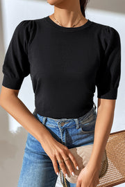 Black knit sweater with puff sleeves and crew neck, styled with jeans.