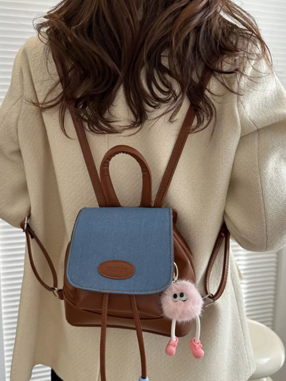 Brown leather mini backpack with blue denim flap and fuzzy pink charm.