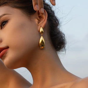 Gold teardrop earrings with a polished finish, dangling from the ear.
