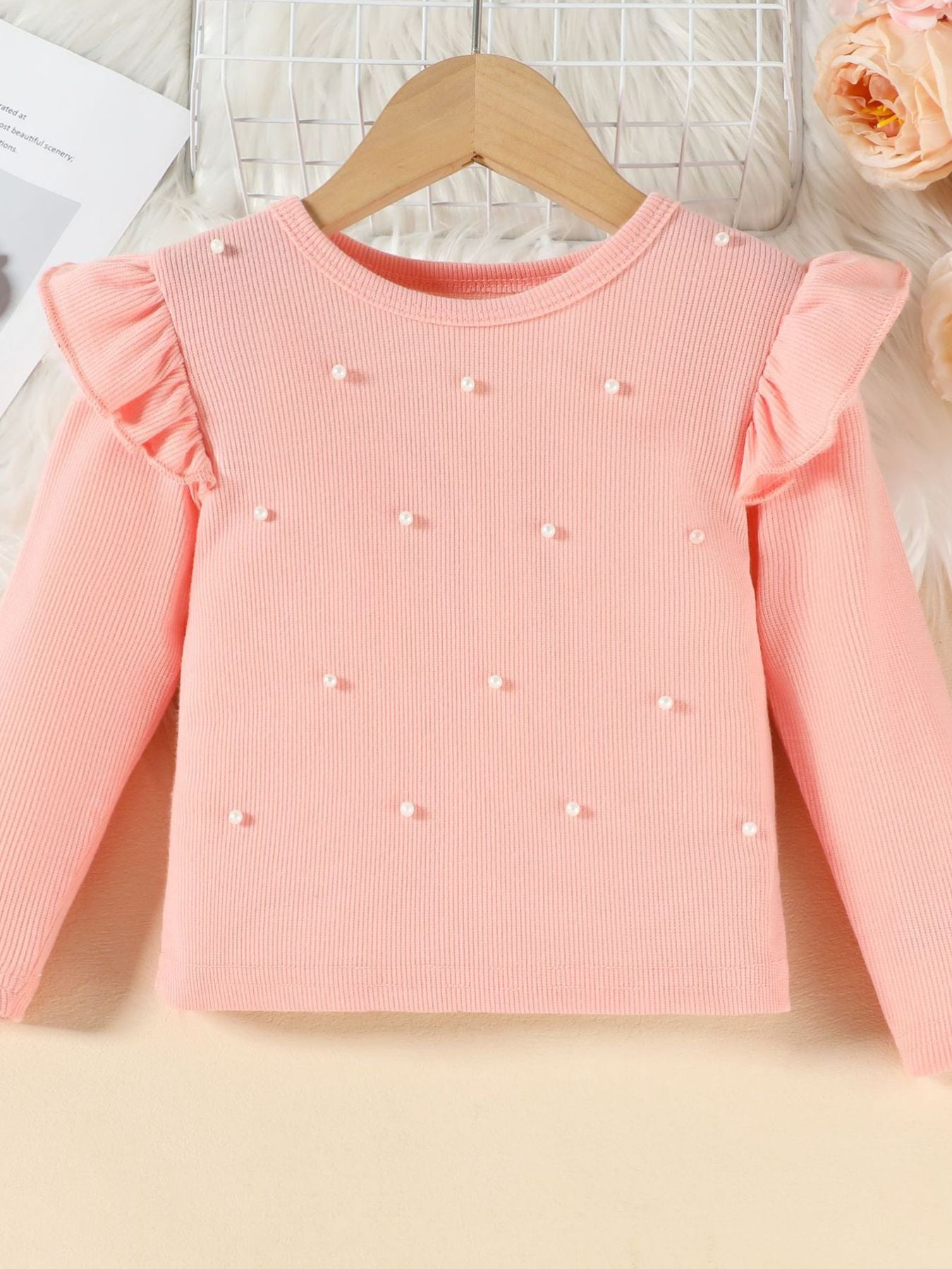 Pink ribbed long sleeve top with pearl embellishments and ruffled shoulders.