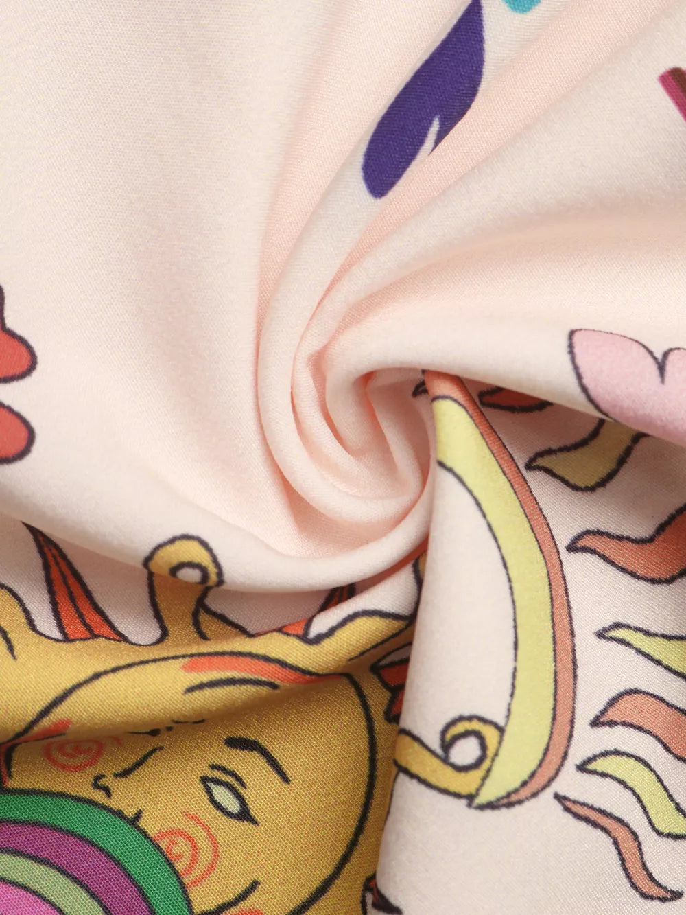 Smocked romper fabric detail with a whimsical sun and rainbow print on a light pink background.