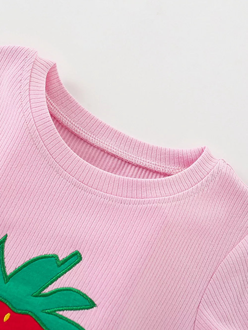 Pink ribbed cotton baby tee with strawberry graphic detail and ruffled shorts.