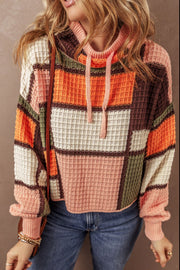 Waffle knit hoodie with colorblock patchwork in orange, pink, cream, brown, and green. Features drawstring hood.