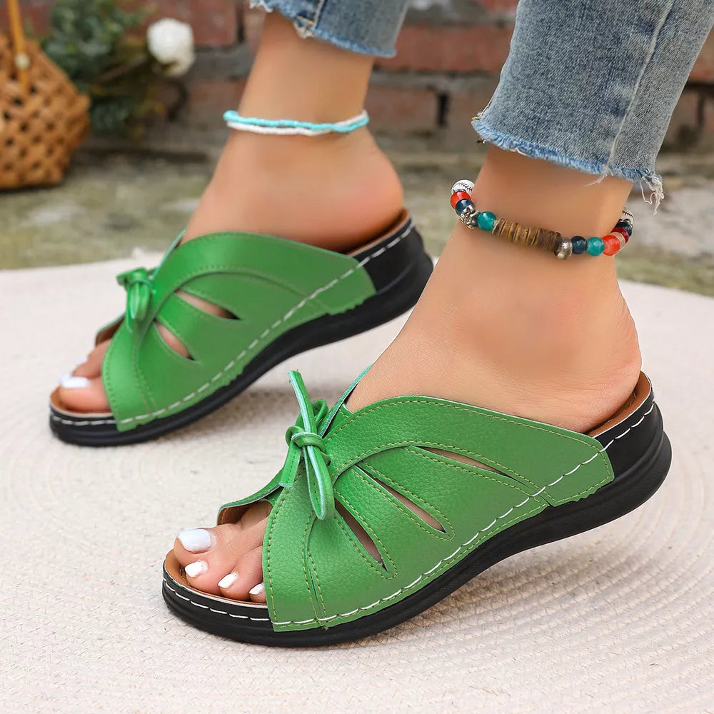 Green leather criss-cross wedge sandals with bow detail and white stitching.