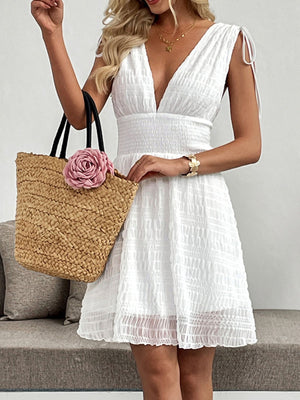 White textured smocked deep V-neck a-line dress with tie shoulder straps, cinched waist, and above-knee length.