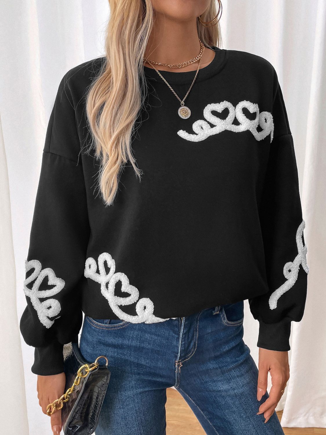 Black sweatshirt with embroidered heart sleeve detail and neckline accent.