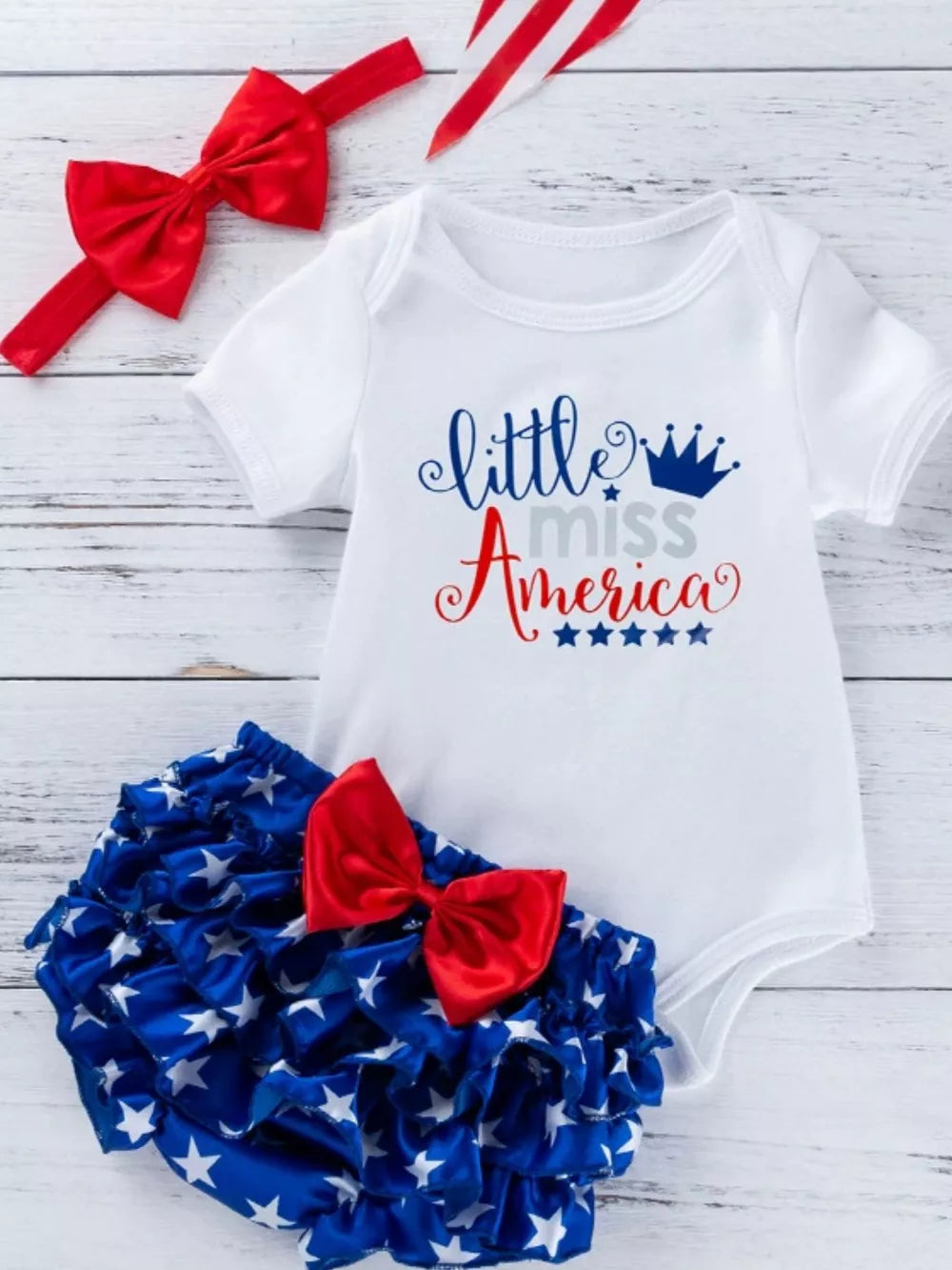 Patriotic baby outfit with white bodysuit and ruffled star bloomer, red bow headband.