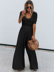 Black textured wide-leg jumpsuit with subtle waist and short sleeves, v-neckline.