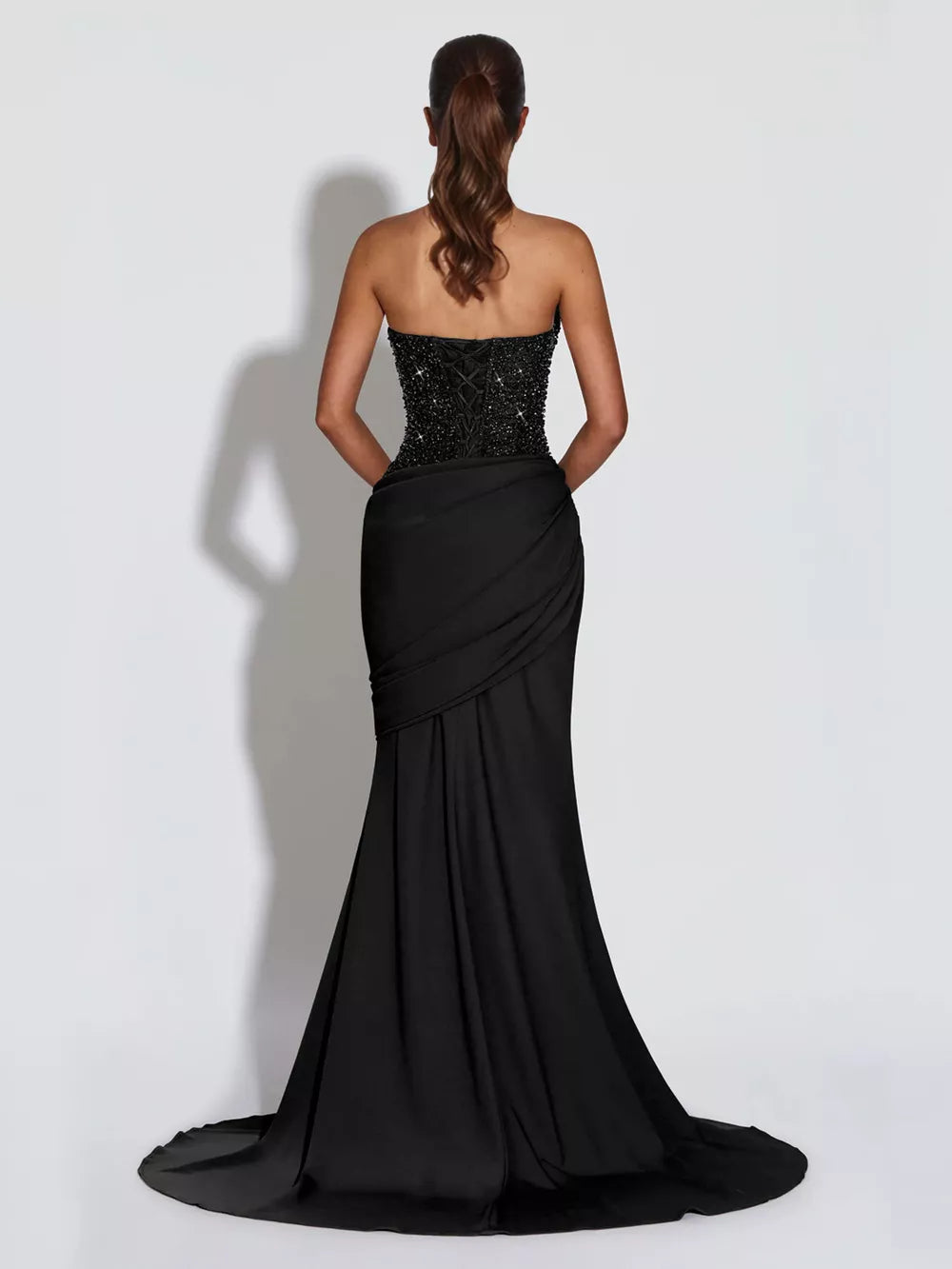 Black sequin corset maxi gown with draped skirt and lace-up back detail.
