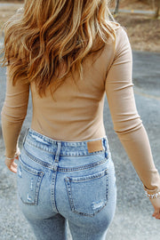 Sand ribbed turtleneck bodysuit with long sleeves, paired with distressed denim jeans.