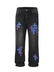 Dark wash denim jeans with embroidered cross patchwork and paint splatters.