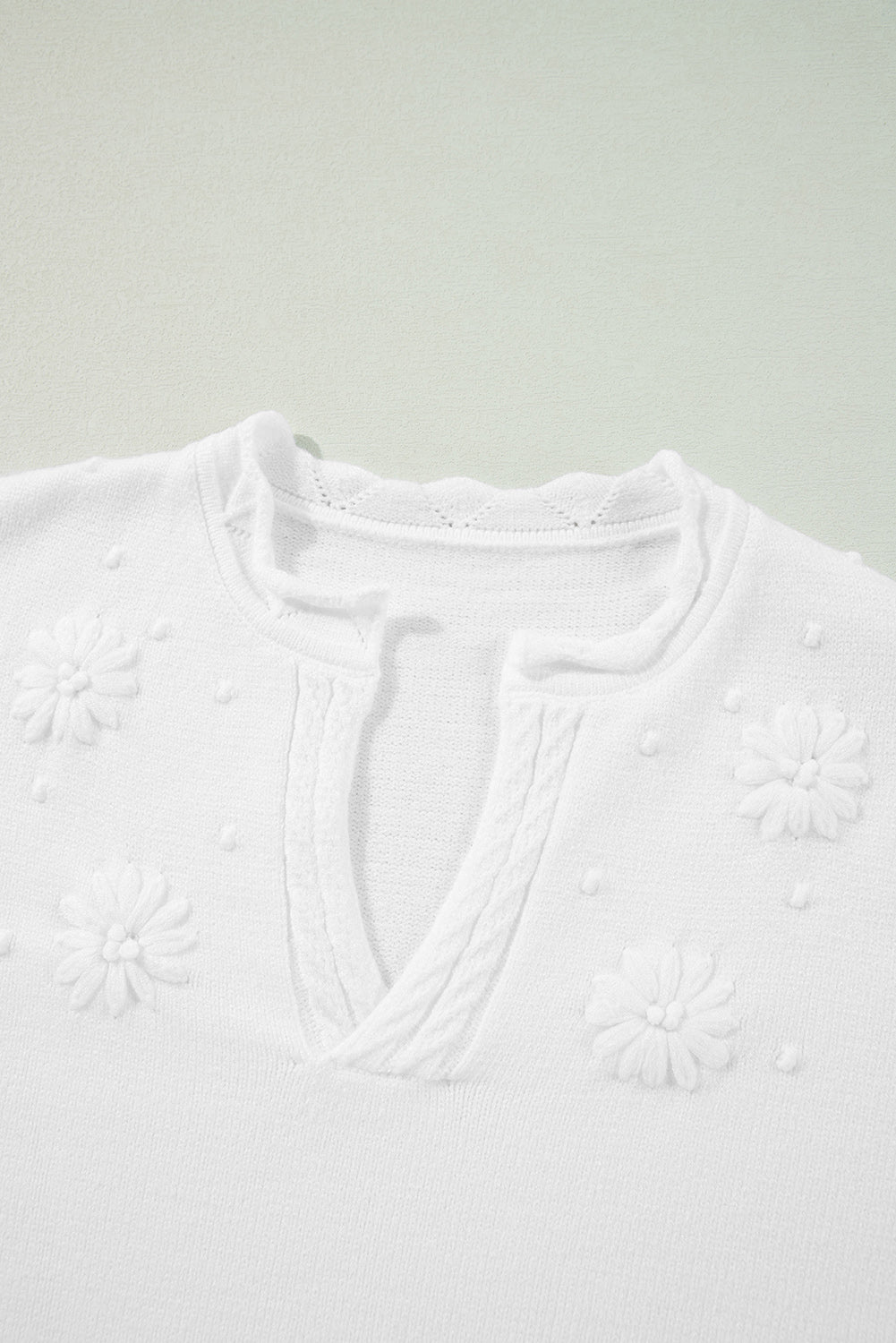 White embroidered floral knit sweater with notch neck and textured details.