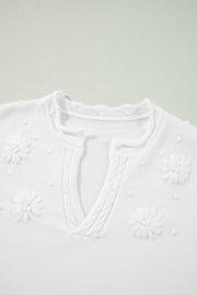 White embroidered floral knit sweater with notch neck and textured details.