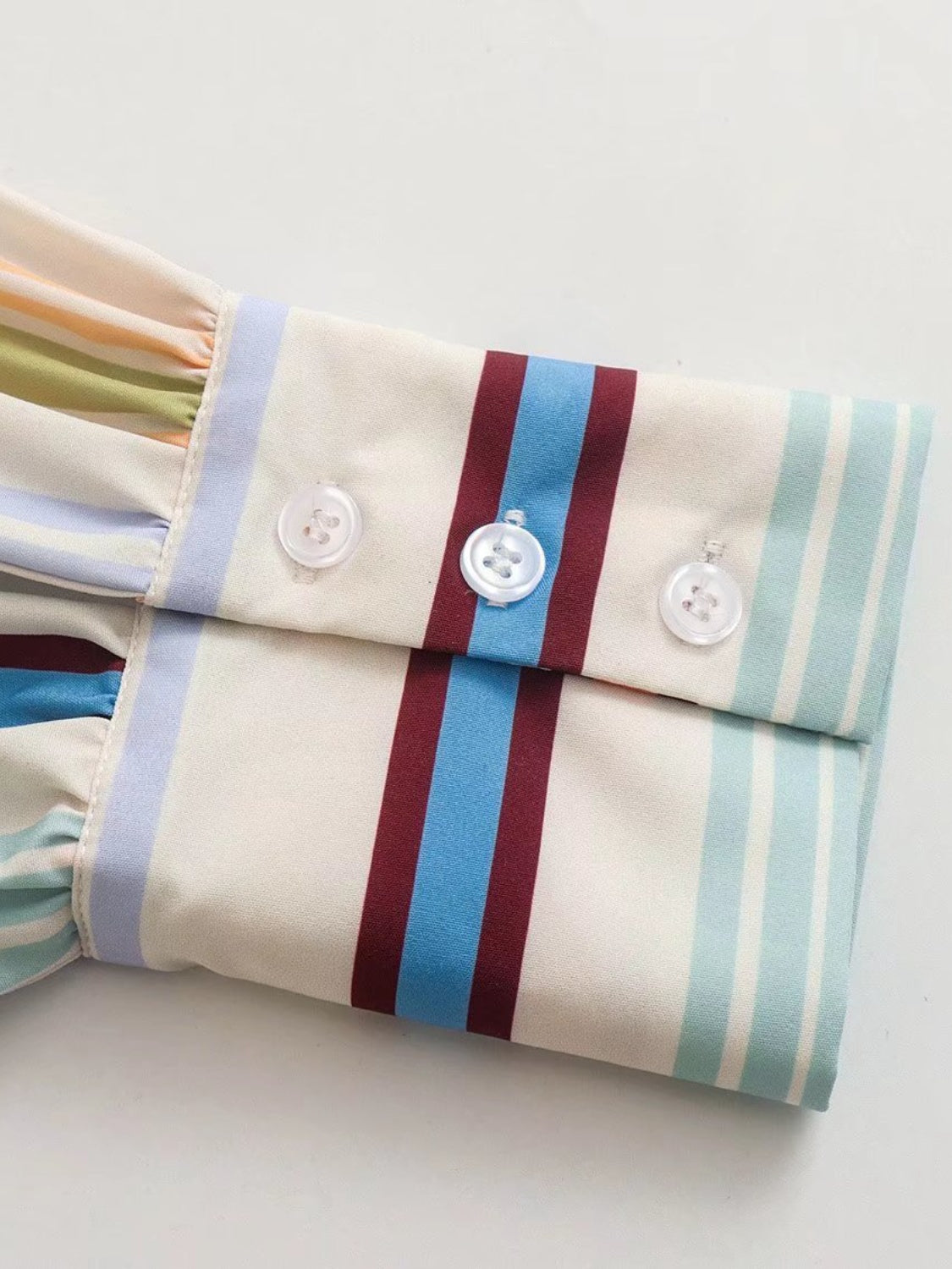 Prismatic stripe band collar blouse with buttoned cuffs and ruffled sleeve detail.