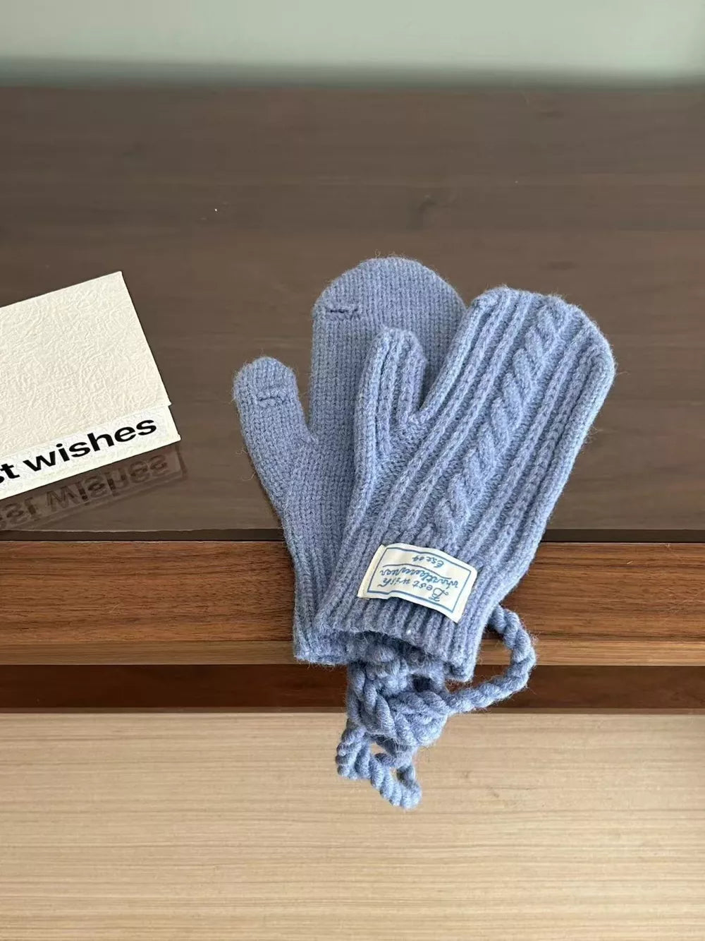 Blue cable knit acrylic gloves with a braided cord and a white label.