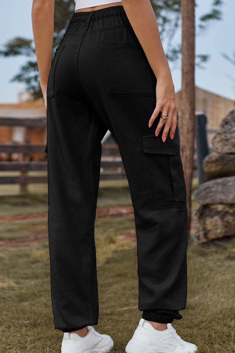 Black cargo pants with multiple pockets and elastic cuffs, styled with white sneakers.
