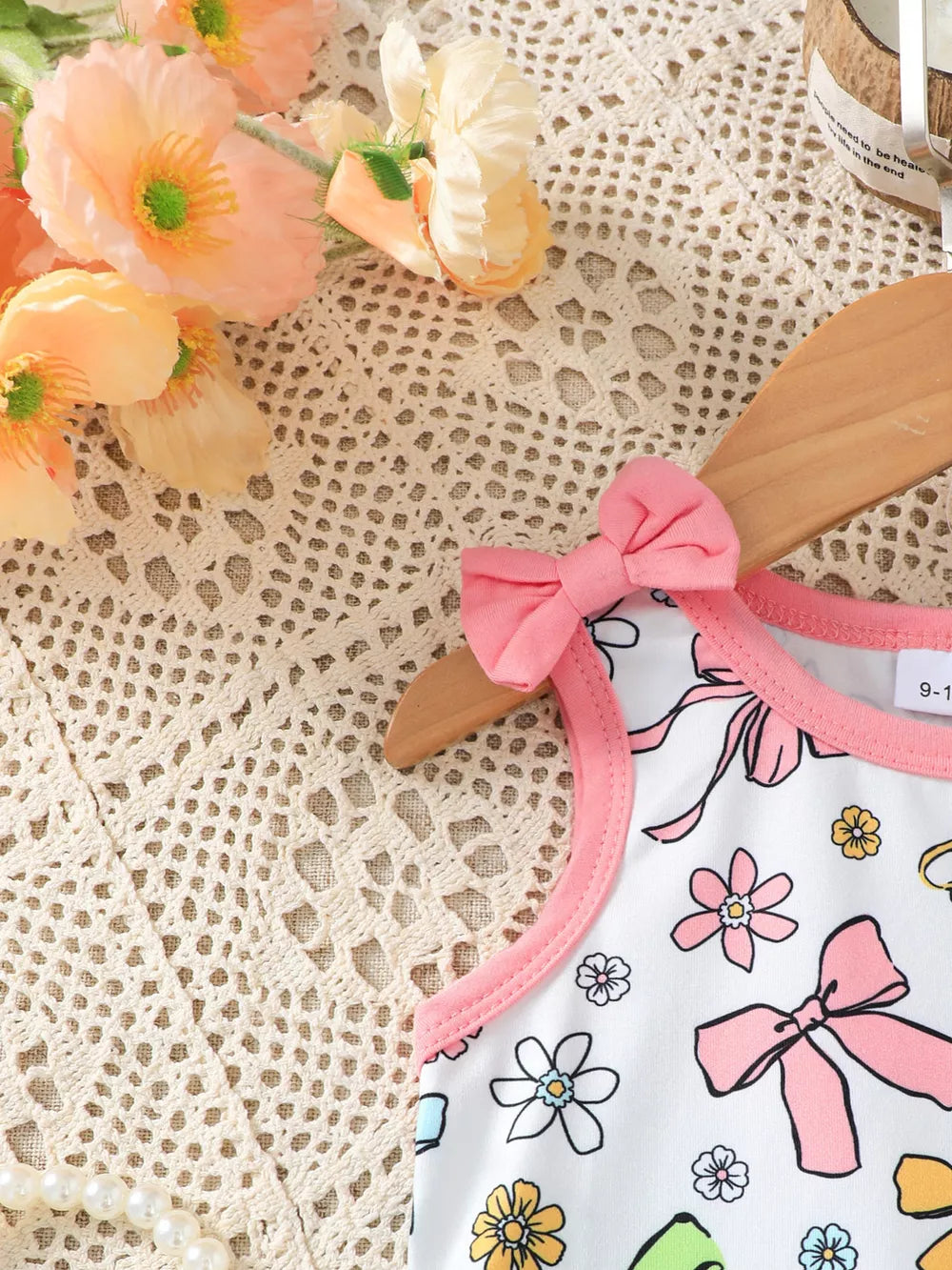 Toddler white one-piece with pink floral and bowknot print, pink trim, and bowknot shoulder detail.