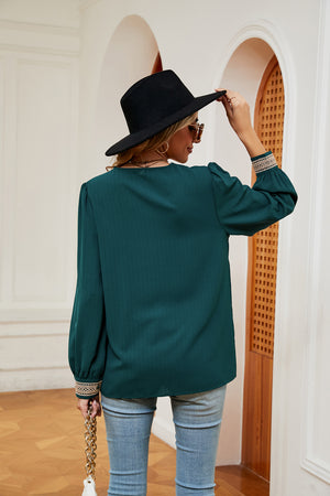 Green blouson top with embroidered trim on sleeves and subtle vertical ribbing.