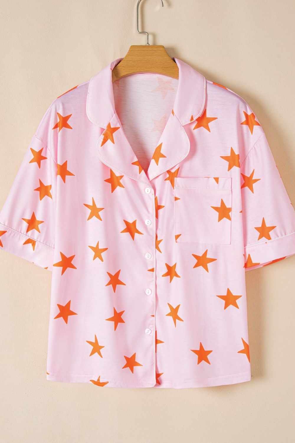 Pink pajama top with orange stars, button front, collar, and chest pocket.
