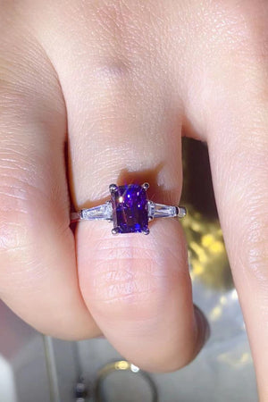 Purple emerald-cut moissanite and baguette platinum ring with accent stones.