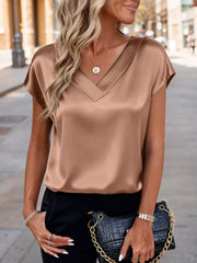 Lustrous satin V-neck blouse in Khaki with short sleeves, styled with a necklace and black pants.
