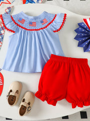 Baby patriotic smocked top with embroidered flags and red trim, paired with red ruffled shorts.