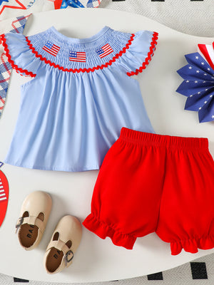 Baby patriotic smocked top with embroidered flags and red trim, paired with red ruffled shorts.