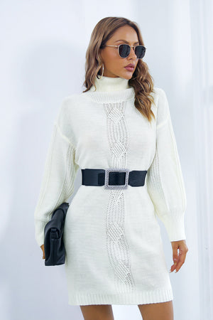 White cable knit turtleneck sweater dress with blouson sleeves and a black jeweled belt.