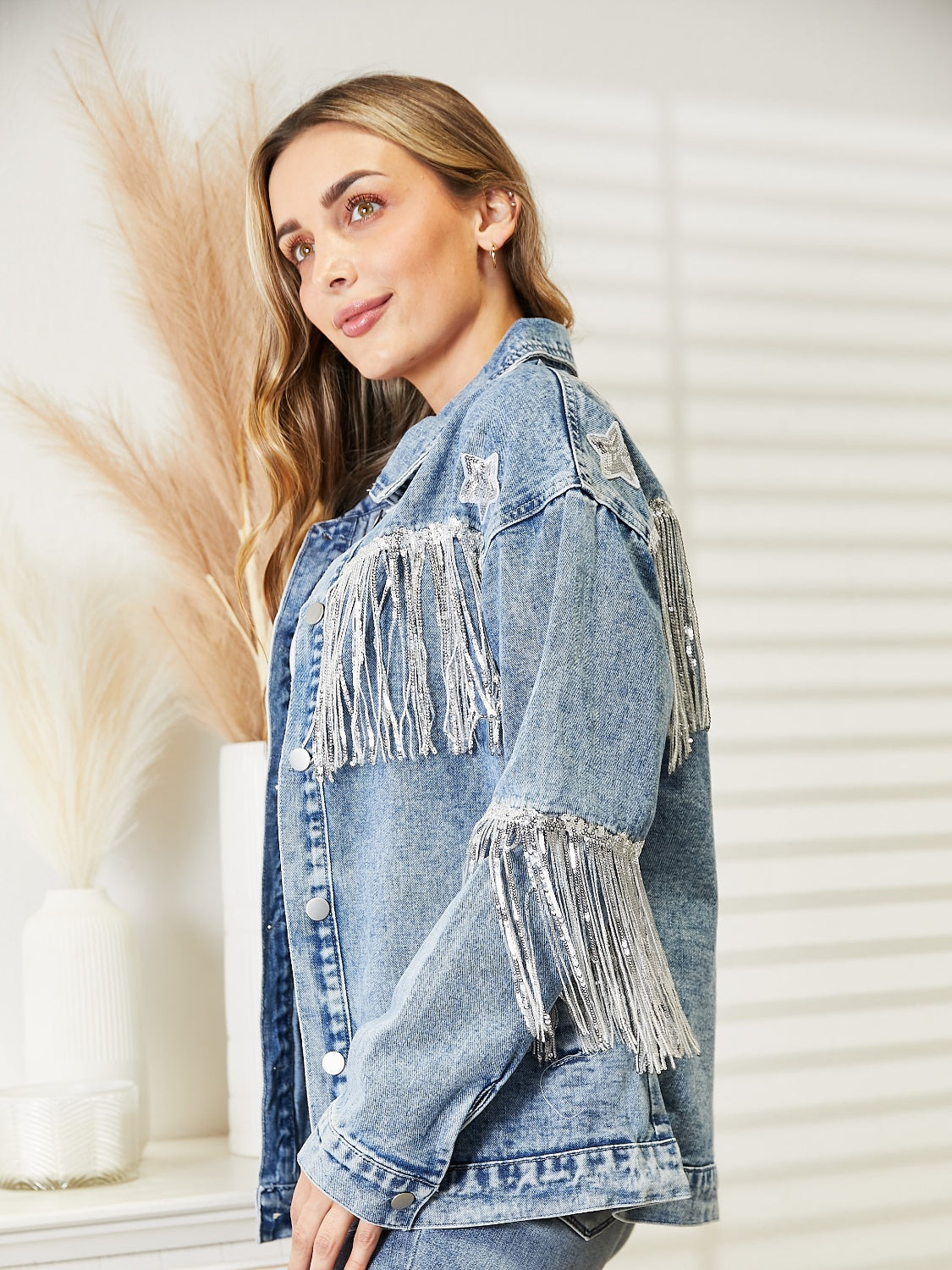 Light wash denim trucker jacket with star patches and silver fringe details on shoulders and cuffs.