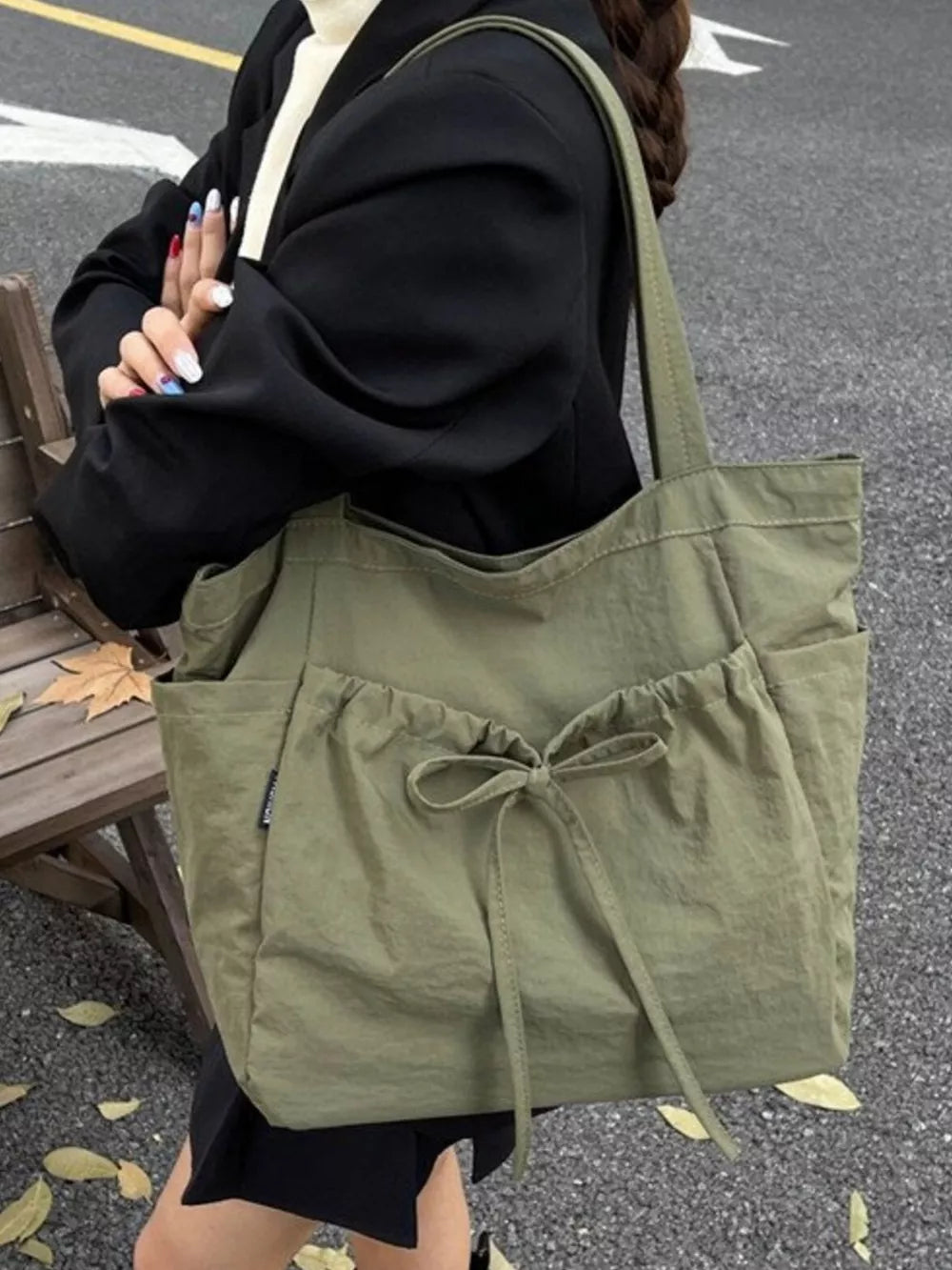 Olive green nylon tote bag with drawstring and bow detail, featuring exterior pockets.
