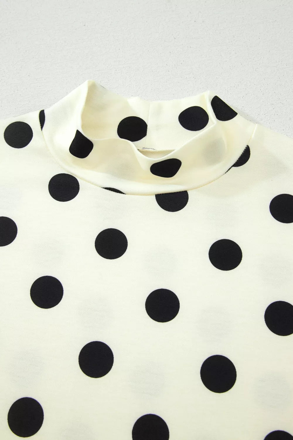 Cream polyester t-shirt with black polka dots and a high neck.