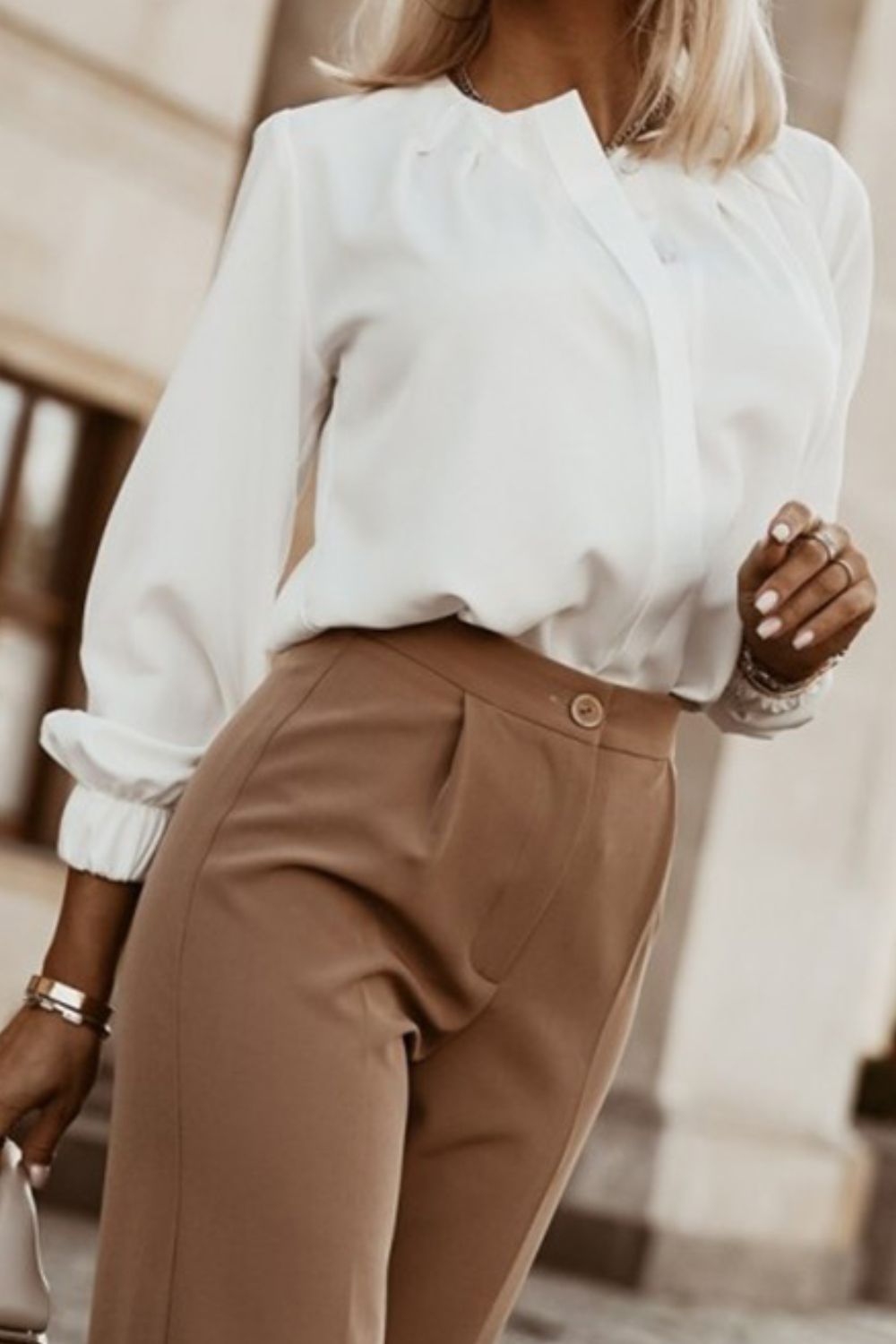 White pleated yoke blouse with button detail and cuffed sleeves styled with khaki trousers.