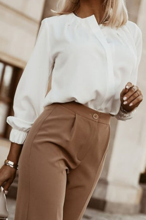 White pleated yoke blouse with button detail and cuffed sleeves styled with khaki trousers.