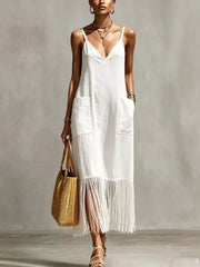 White maxi dress with V-neck, spaghetti straps, pockets, and fringe hem detail.