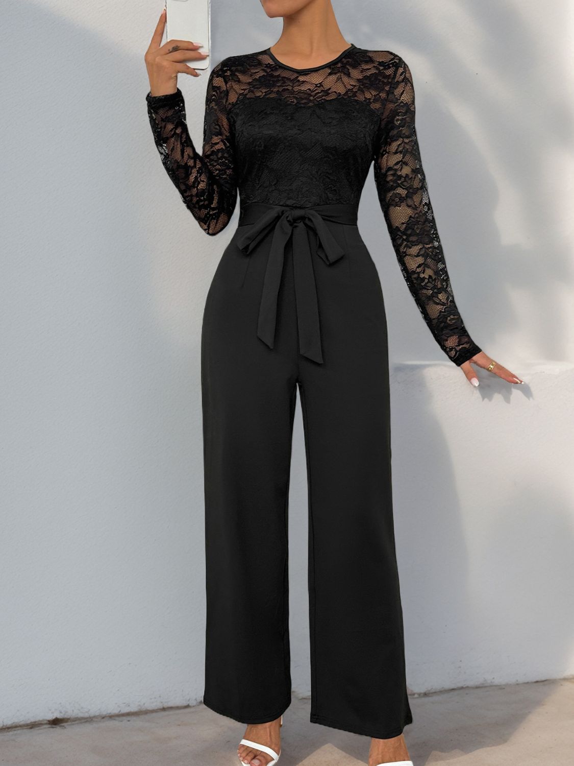 Black lace bodice wide-leg jumpsuit with long sleeves and a tie waist.