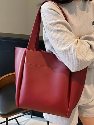 Wine red pu leather tote bag with exterior pocket, worn by a woman.
