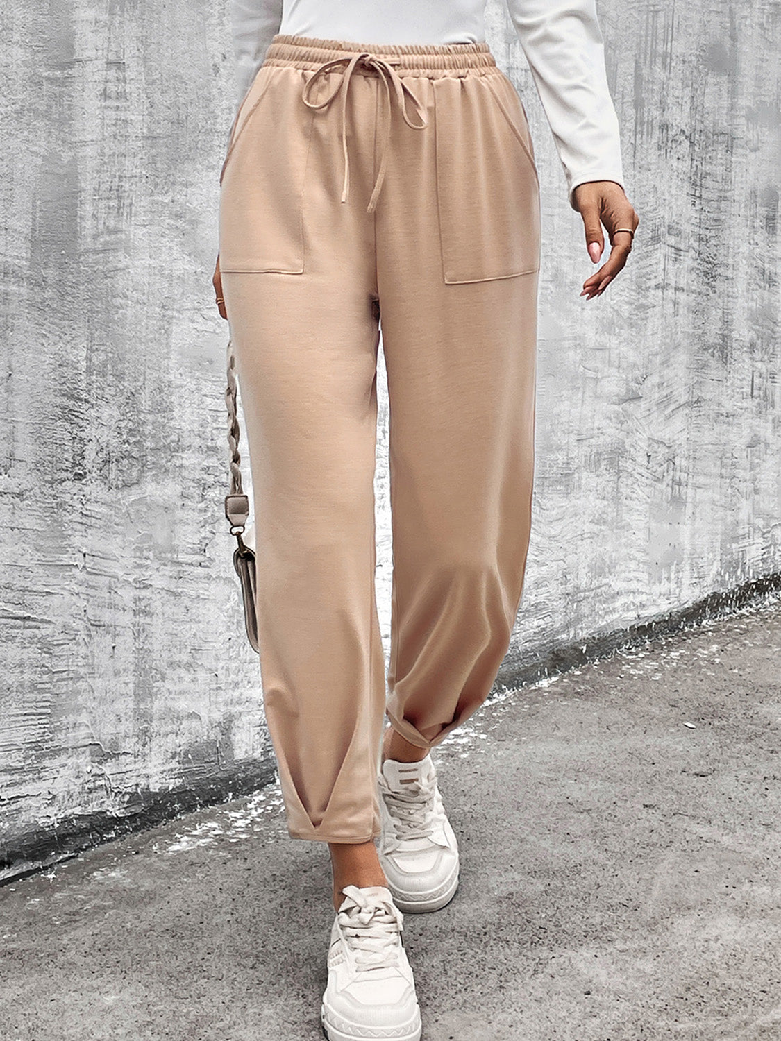 Beige tapered hem utility joggers with drawstring waist and front pockets, styled with white sneakers.